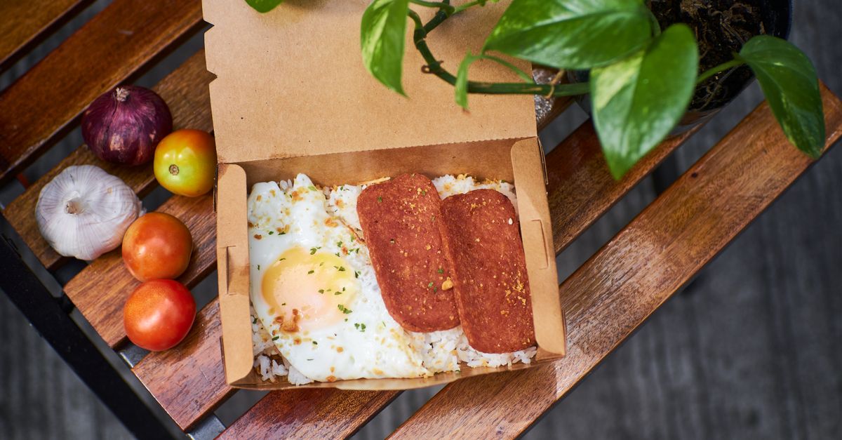 Delicious breakfast box featuring fried egg, sliced meat, and fresh vegetables on a rustic wooden table.